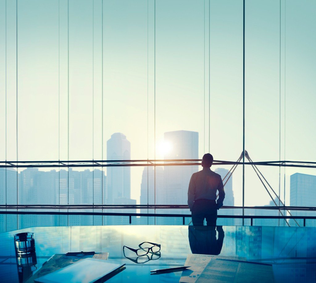 Business professional overlooking a city skyline at sunrise from a high-rise office